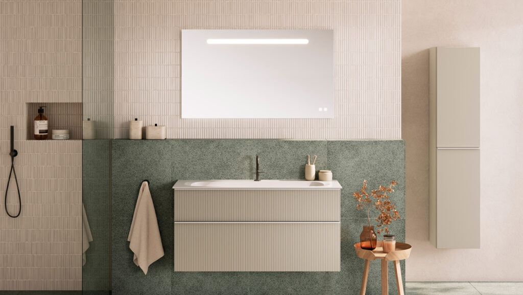 Modernes Badezimmer mit einem rechteckigen Spiegel über einem Waschbecken und einem Waschtisch, sanften grünen und beigen Fliesen, einem Einbauschrank, einem Handtuchhalter und dekorativen Gegenständen wie einer kleinen Vase mit getrockneten Zweigen.