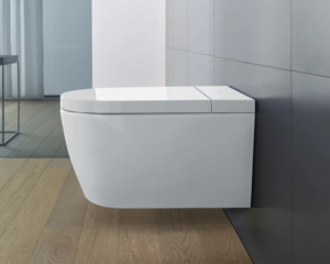 Eine moderne, weiße Wandtoilette ist an einer glatten, grauen Badezimmerwand befestigt. Der Boden ist aus hellem Holz und der Raum ist minimalistisch eingerichtet.